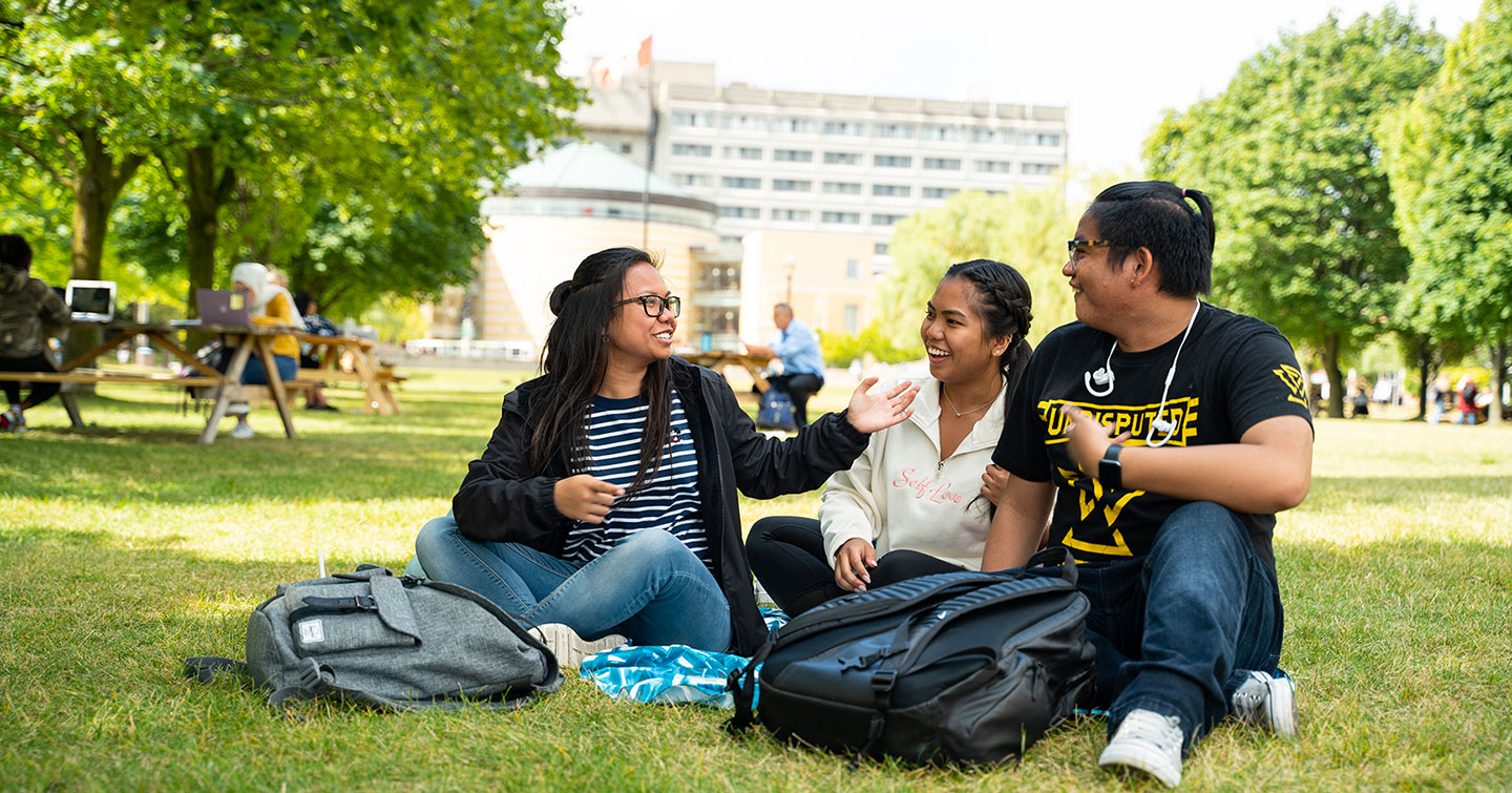 three diverse students laughing while sitting on grass