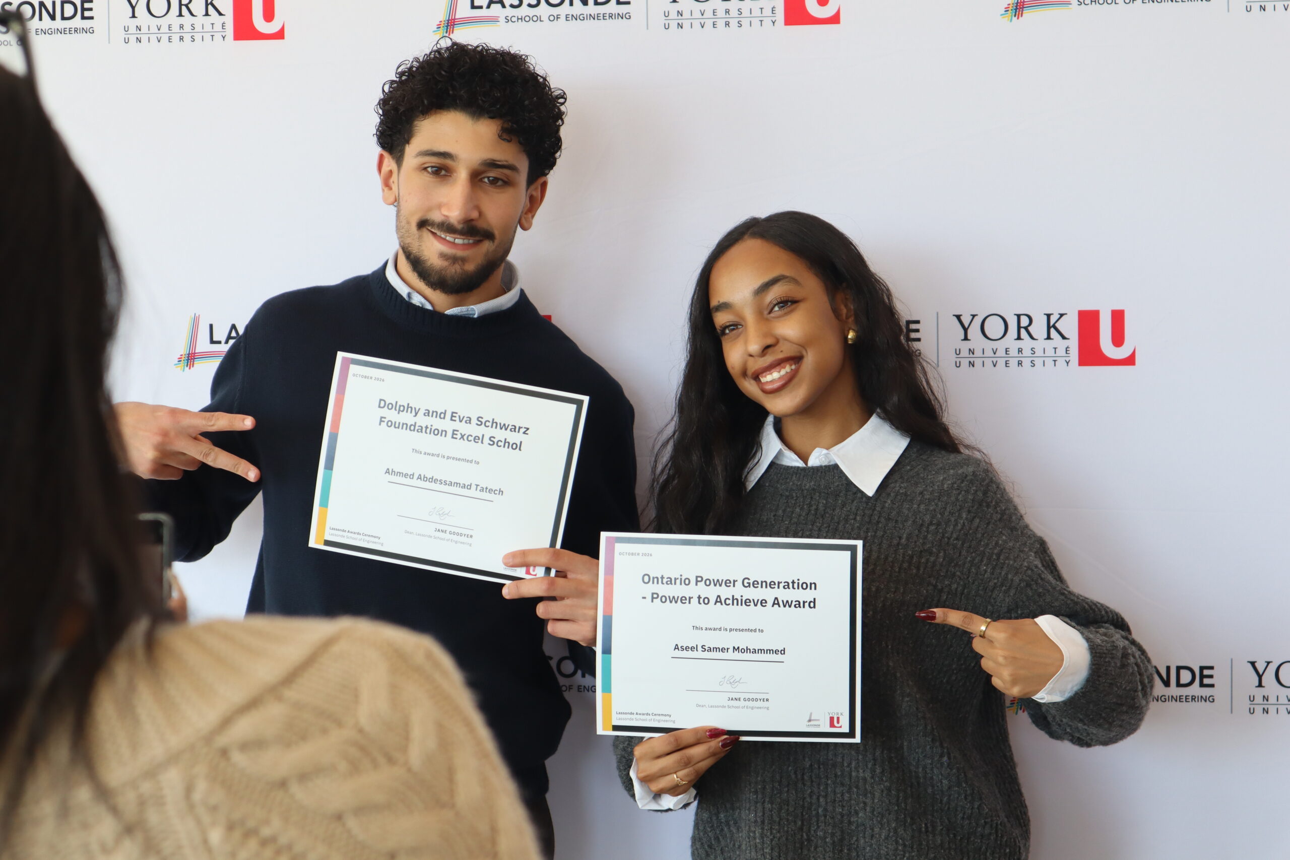 Ahmed Abdessamad Tatech and Aseel Samer Mohammed stand in front of a Lassonde School of Engineering and York University backdrop, each pointing to their award certificates.