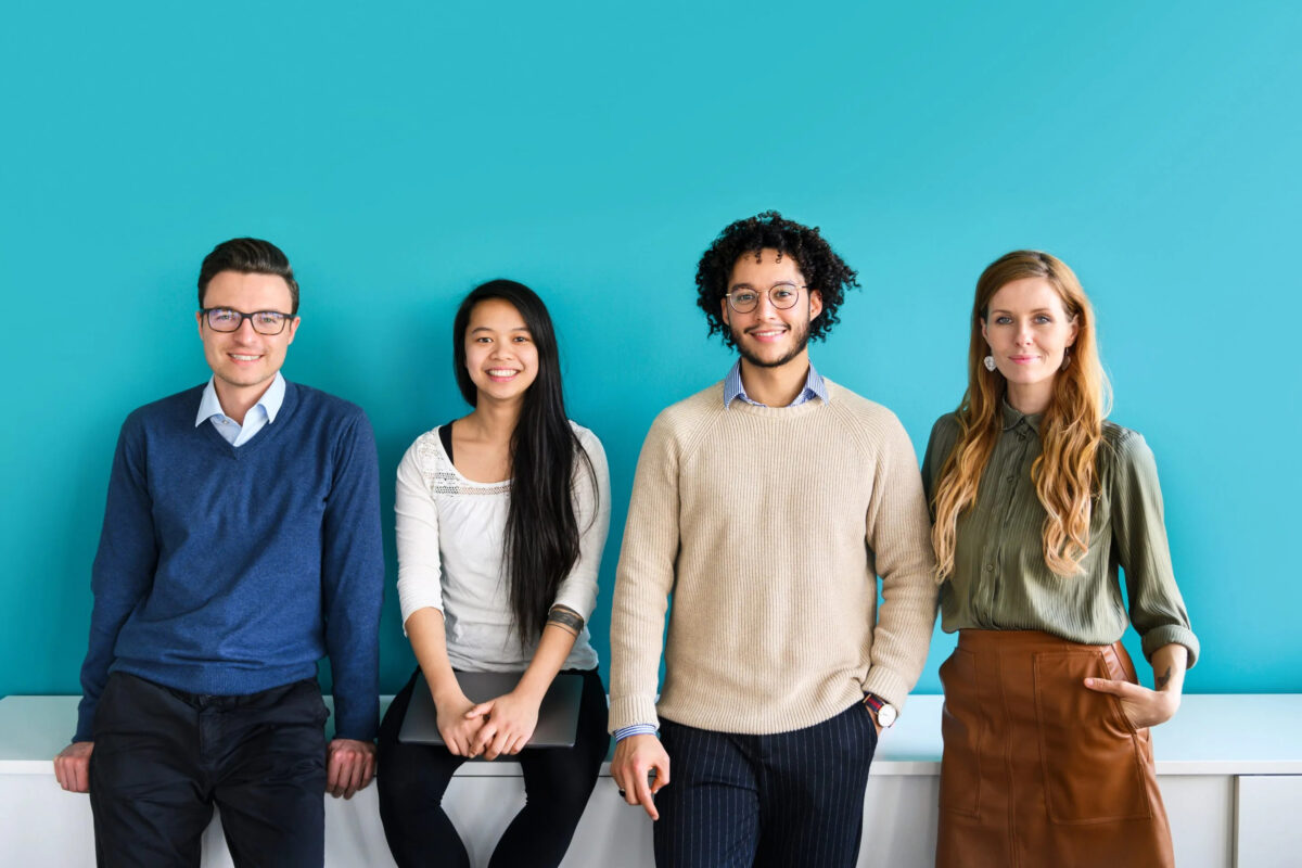 diverse young employees in office clothes, team of four smiling, on turquoise background
