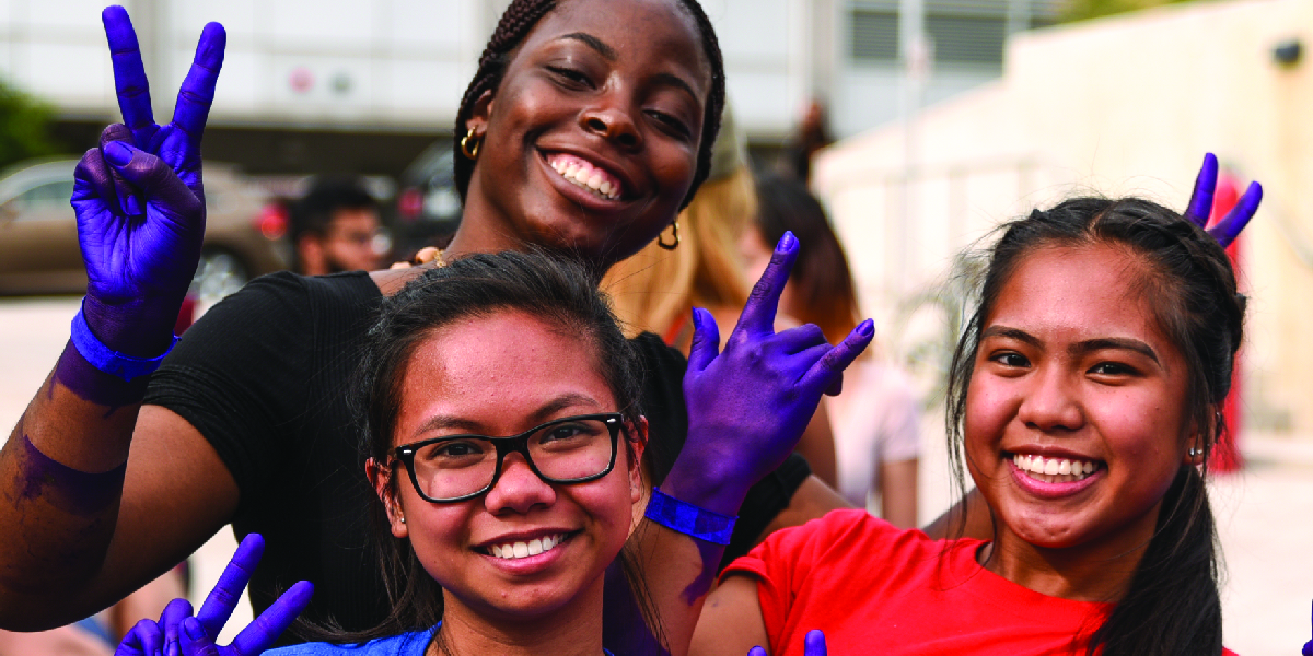 Three students smiling, hands painted purple