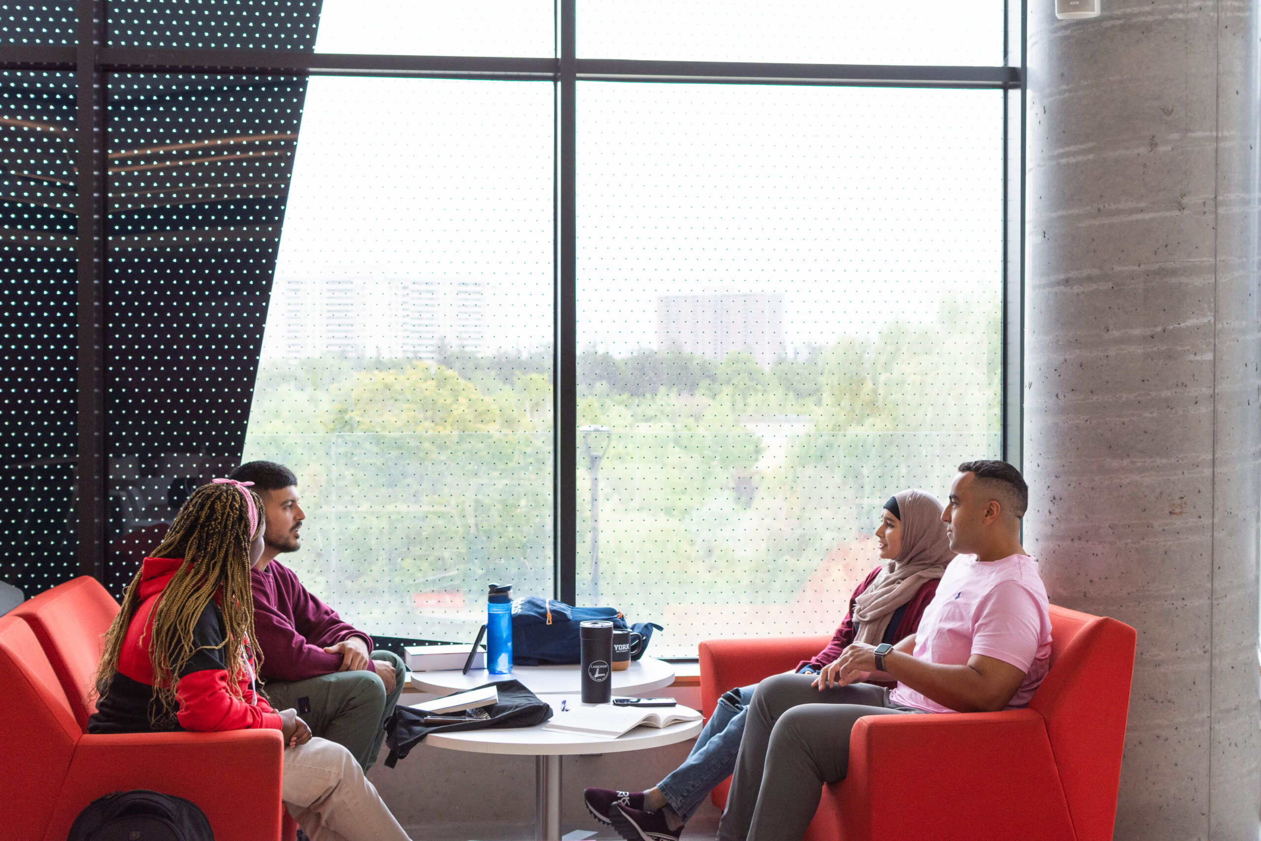 four Lassonde students, sitting on red sofas, having a meeting, chatting