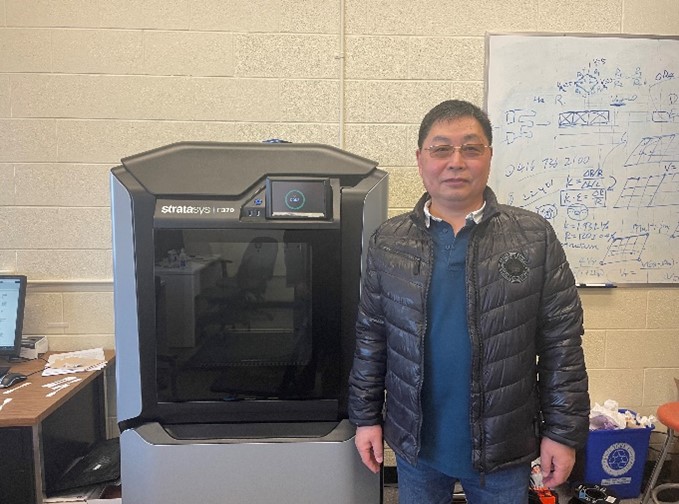 George Zhu standing in front of a fused deposition modeling 3D printer