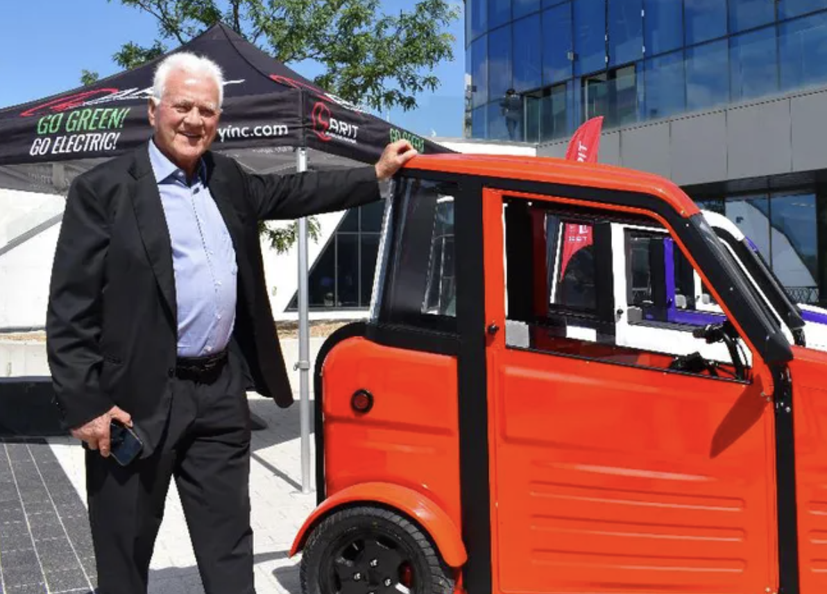 A photo of Frank Stronach standing beside a red SARIT vehicle. 