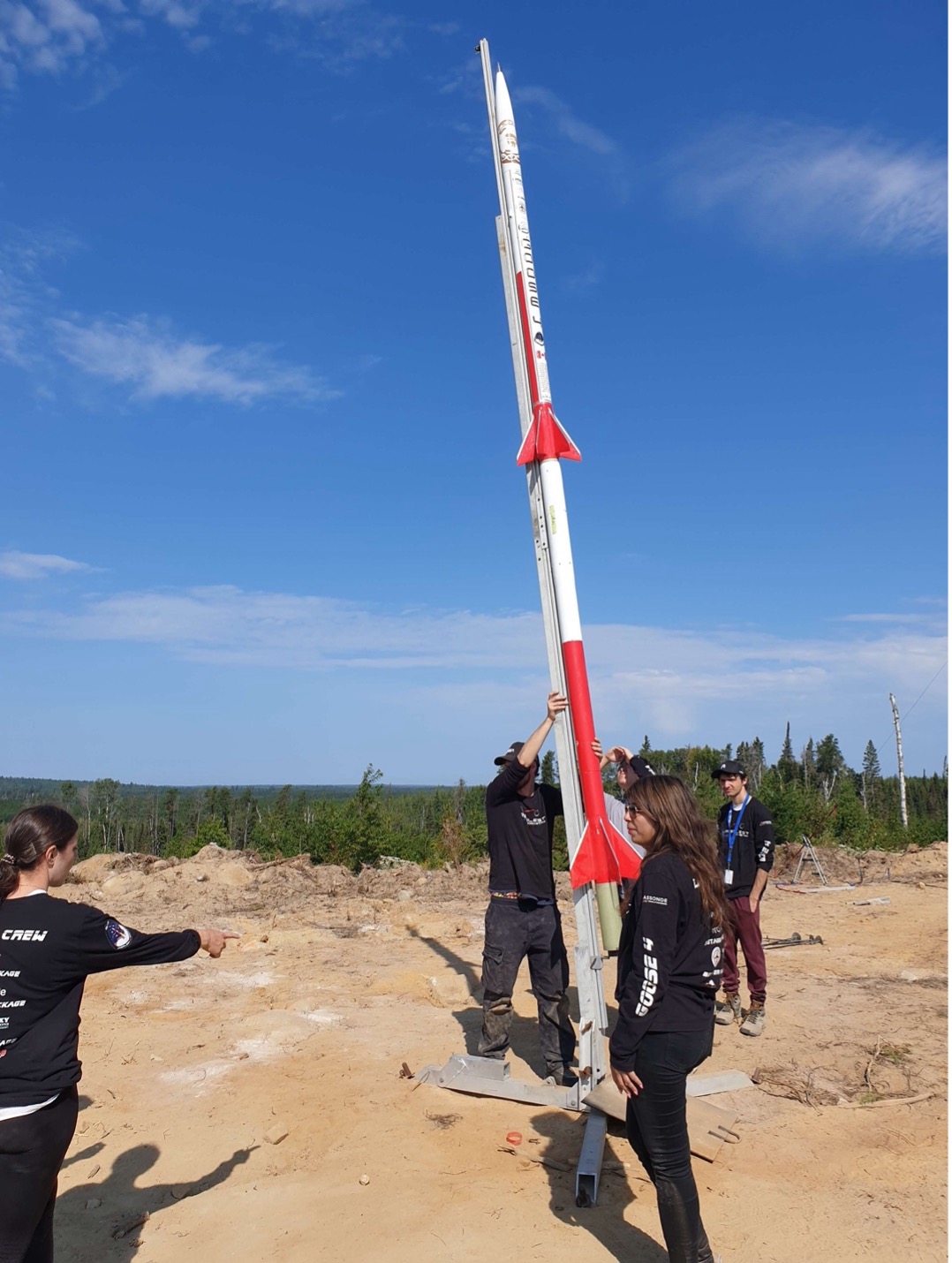Arbalest Rocketry team members preparing tall rocket for launch outdoors