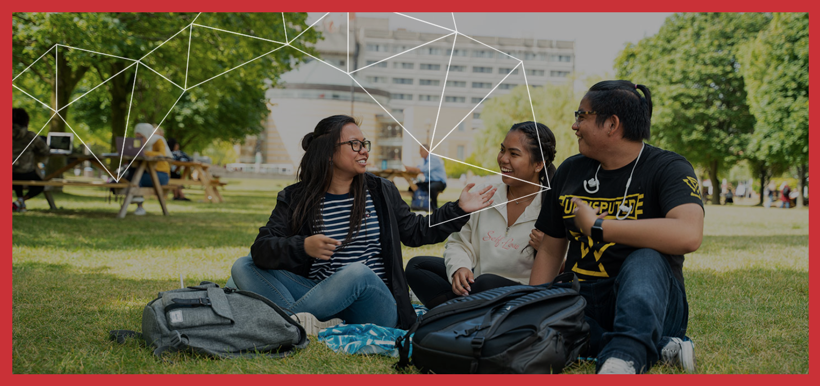 a group of three students sitting on the campus grass spending time together outdoors