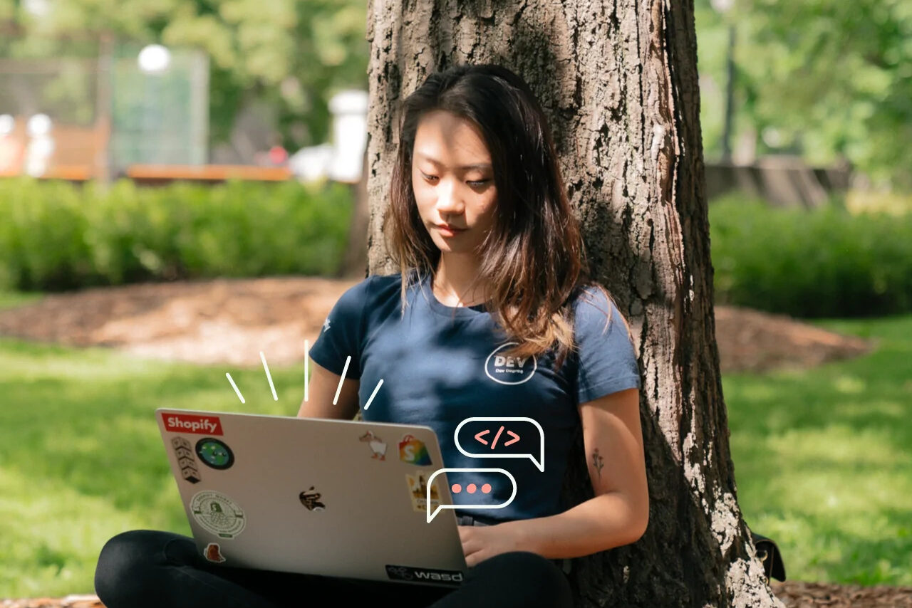 Young woman sitting in grass with laptop, leaning against a tree