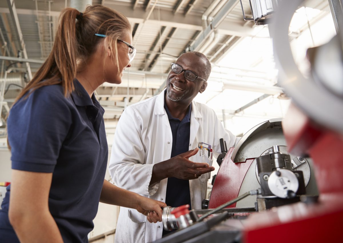 Engineer talking to female apprentice by machinery