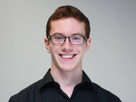 a headshot of a man in a black shirt and glasses, smiling at the camera