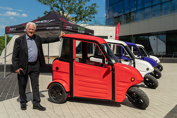 Frank Stronach standing beside a SARIT Electric Vehicle