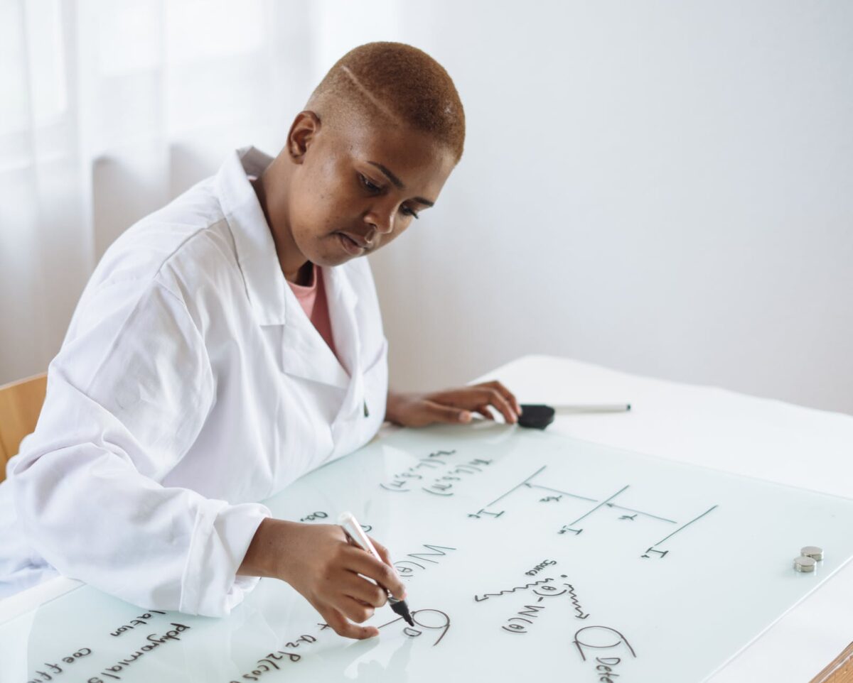 Woman works on equations on white board.