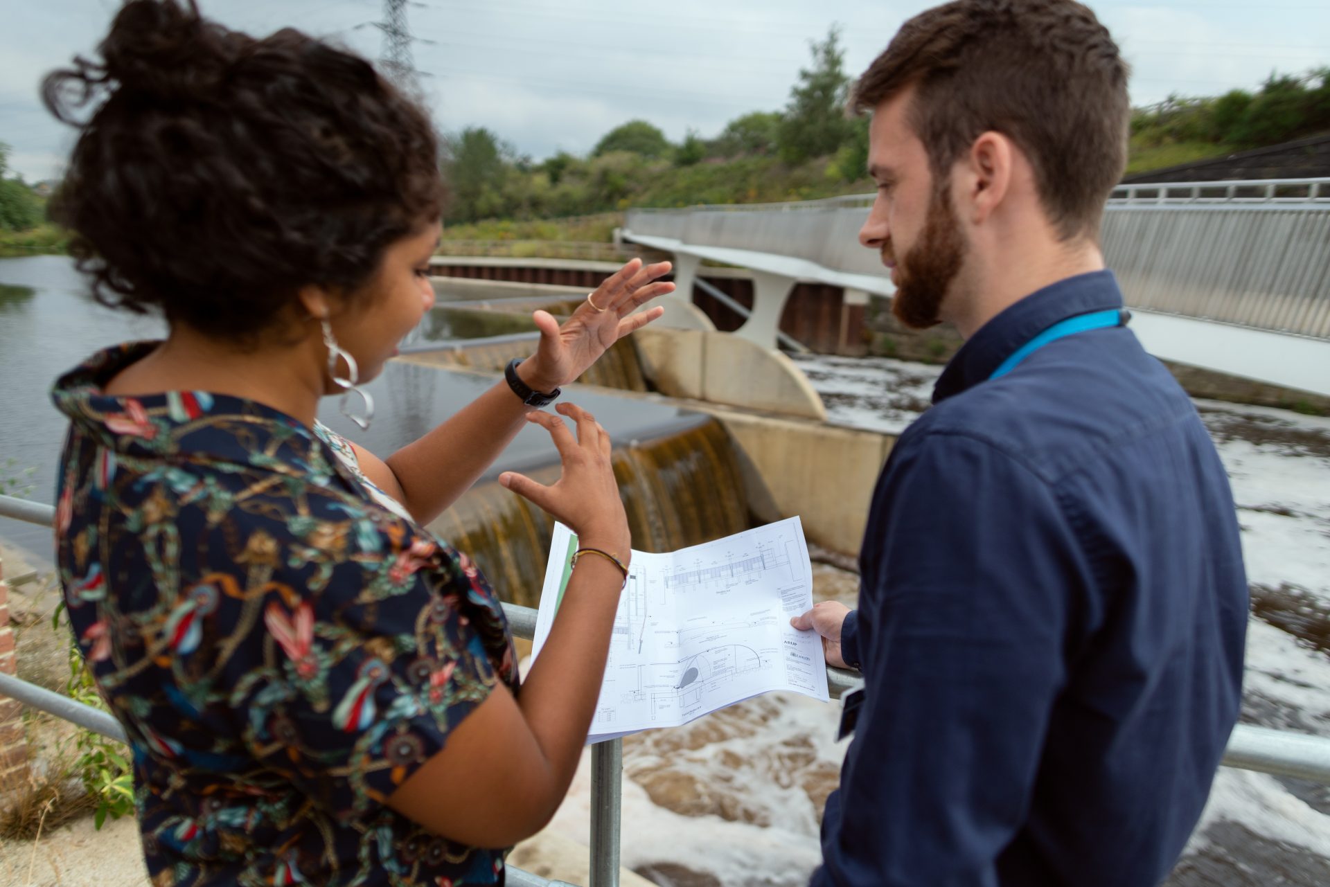 Two people look at schematics in front of a dam